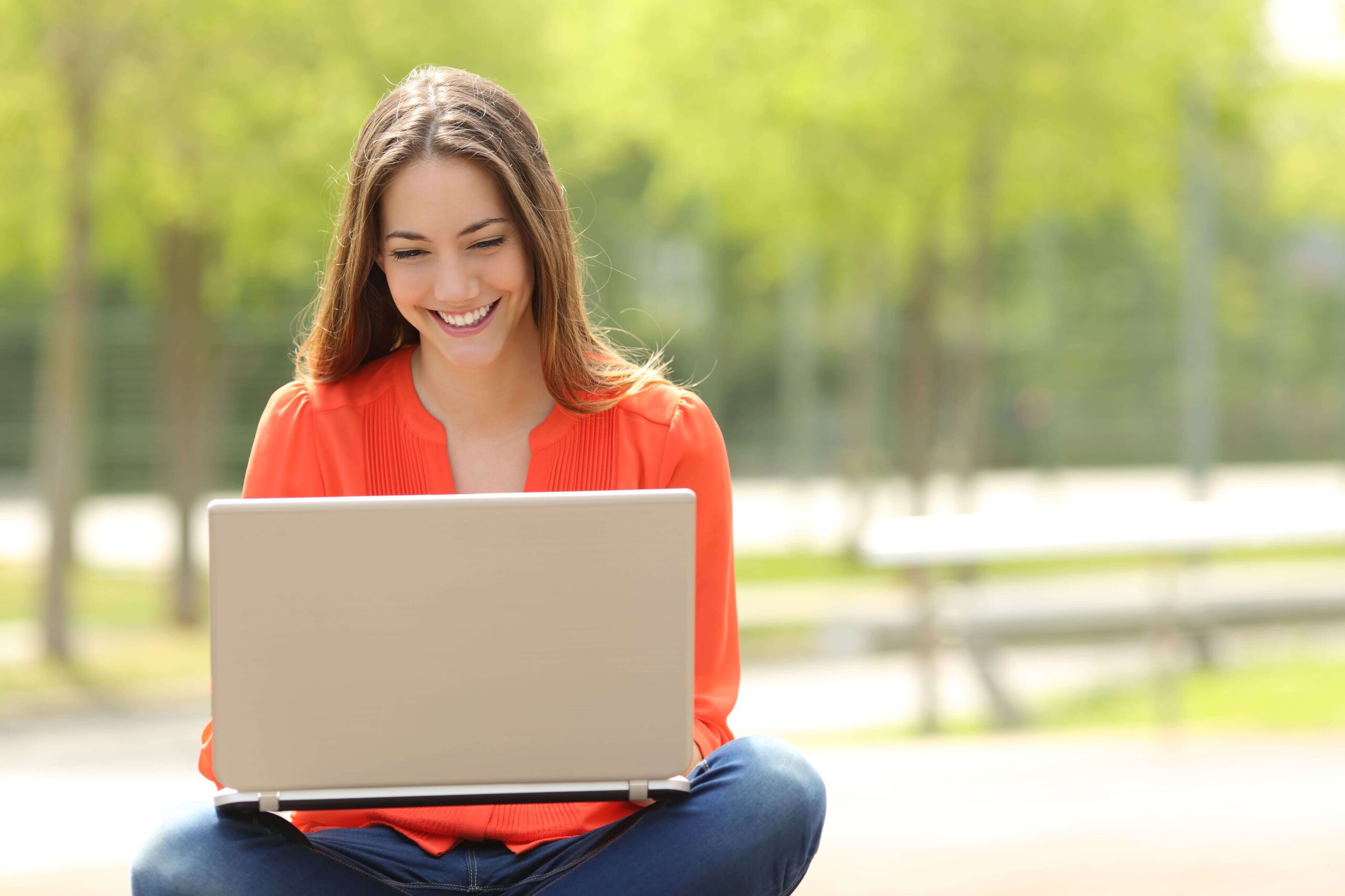 Mujer sonriendo frente a un portatil al aire libre
