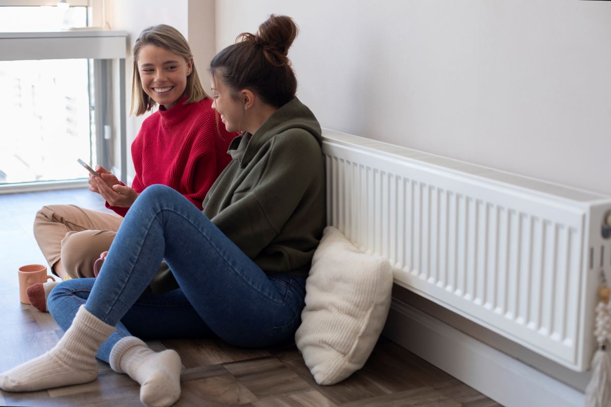 mujeres sonriendo mirando el movil sentadas en el suelo cerca del radiador mirando la tarifa por uso gas naturgy