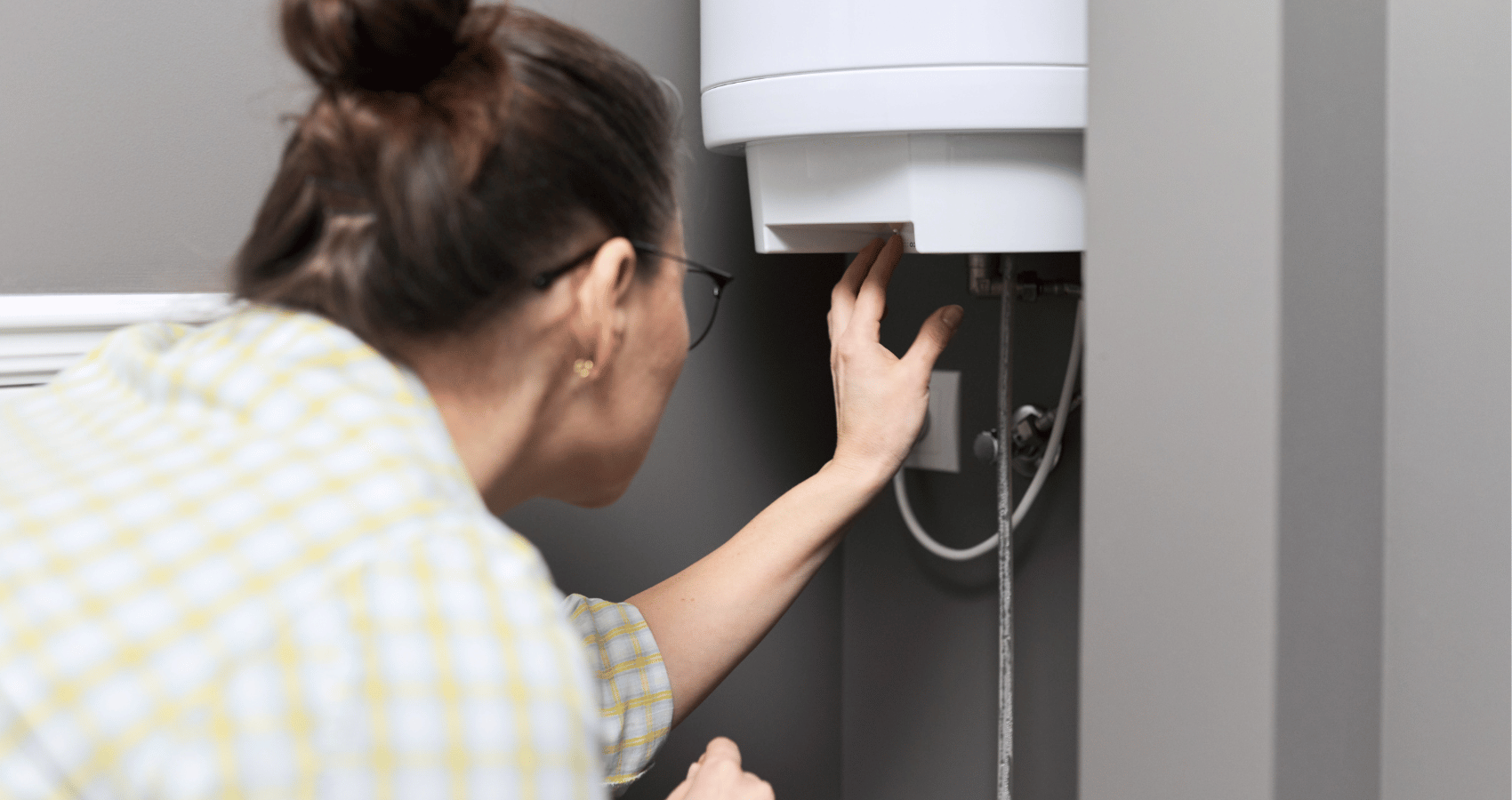 Mujer ajustando la temperatura de un termo electrico o calentador de agua en casa